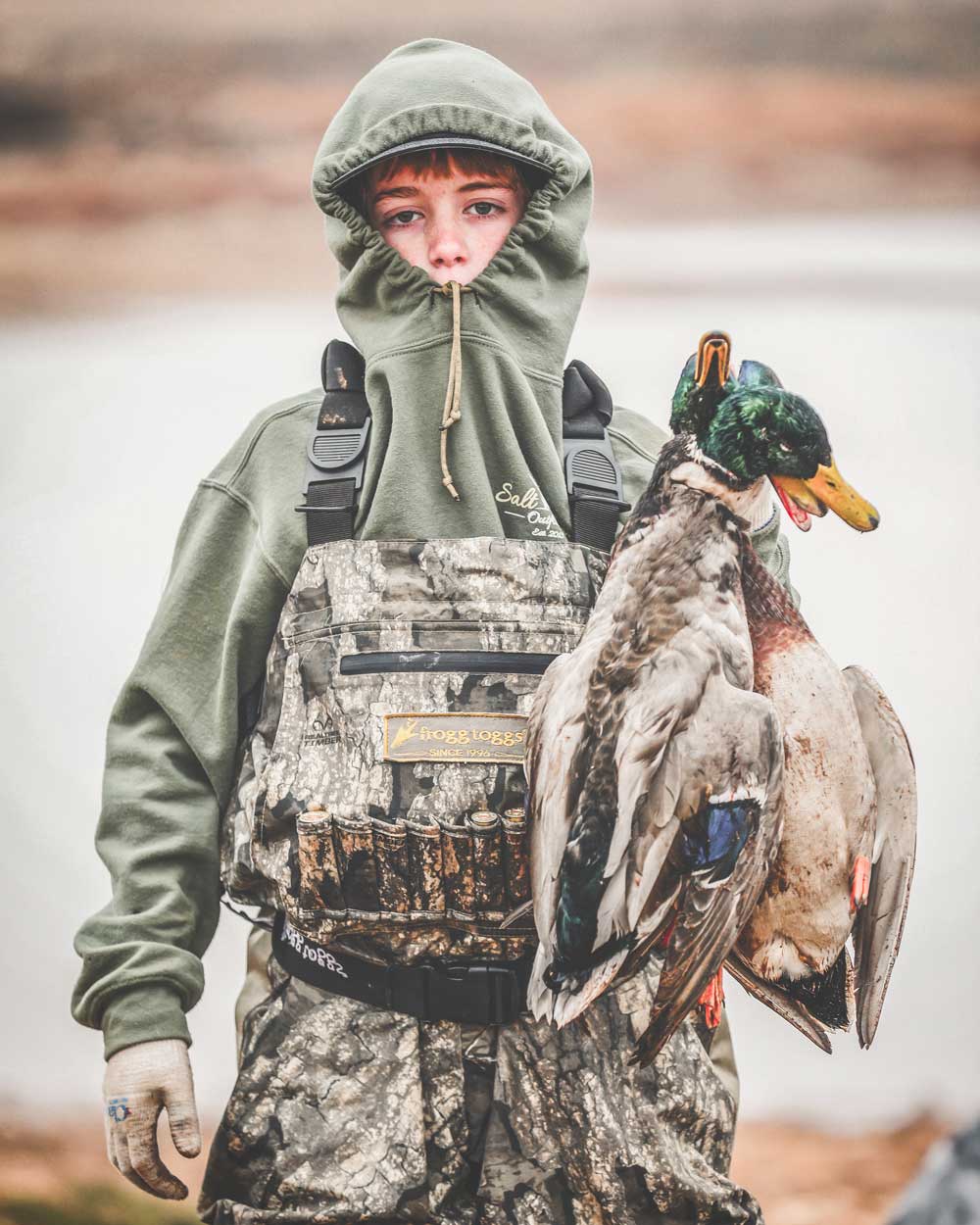 Boy wearing camo waders and holding mallard ducks