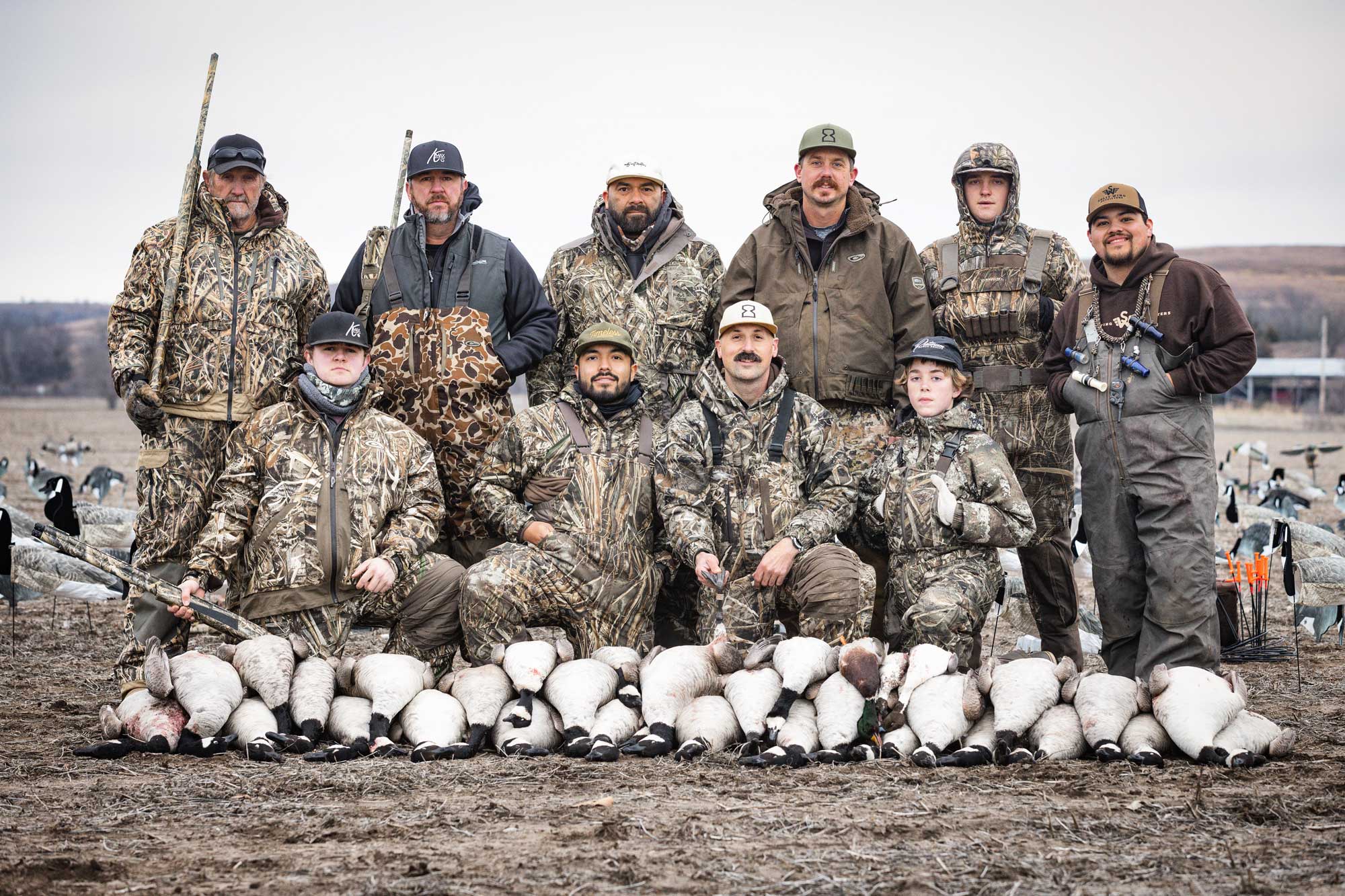 Group of seven hunters in camo standing behind their line of ducks they caught
