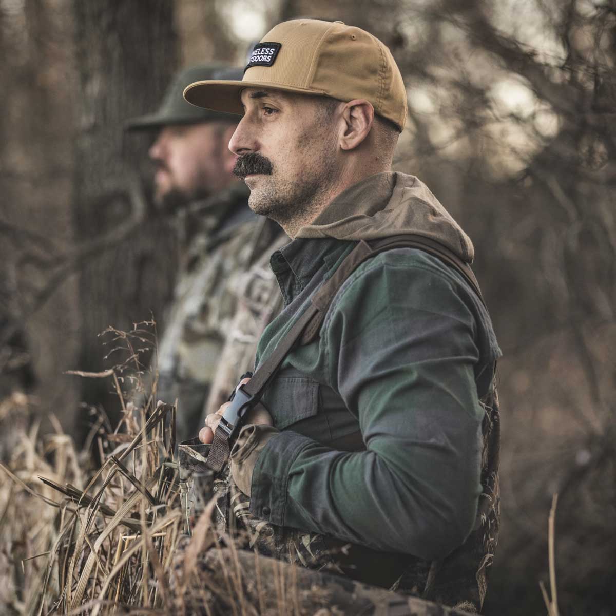 Two men wearing camo standing in the woods, looking off into the distance