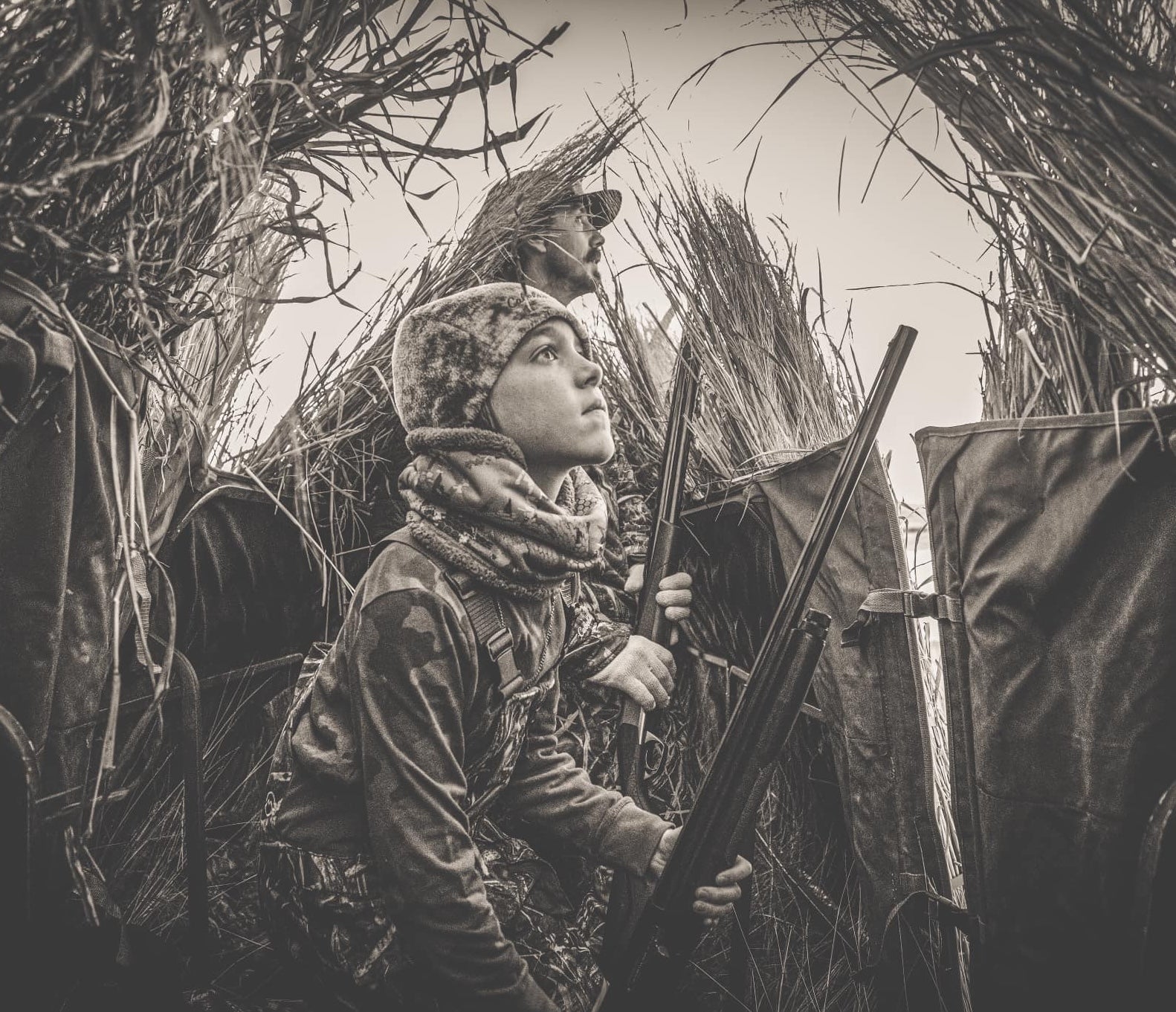 Father and son sitting in a hunting blind holding shotguns