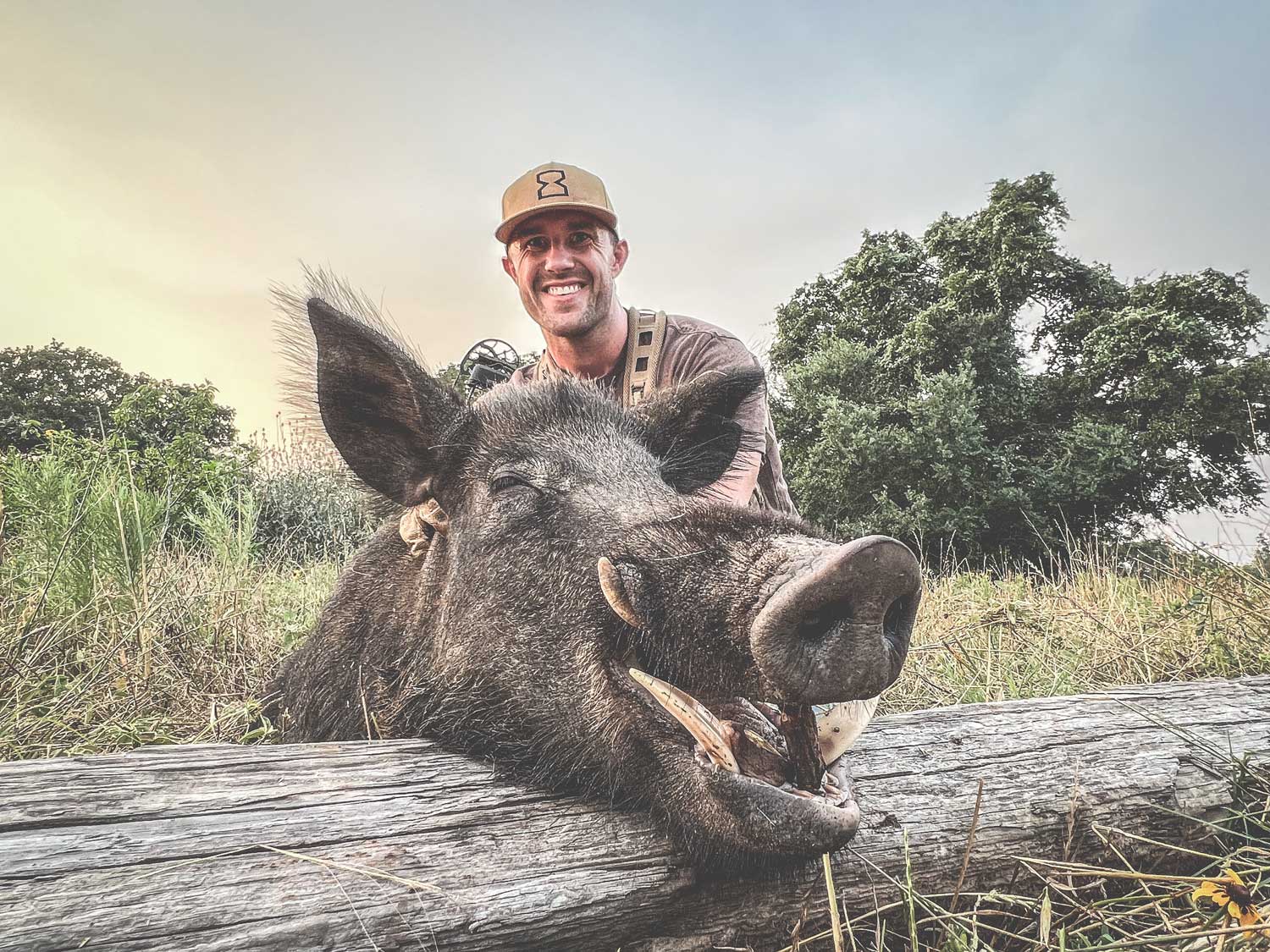 man wearing Timeless Outdoors hat showing off a wild hog he shot while hunting