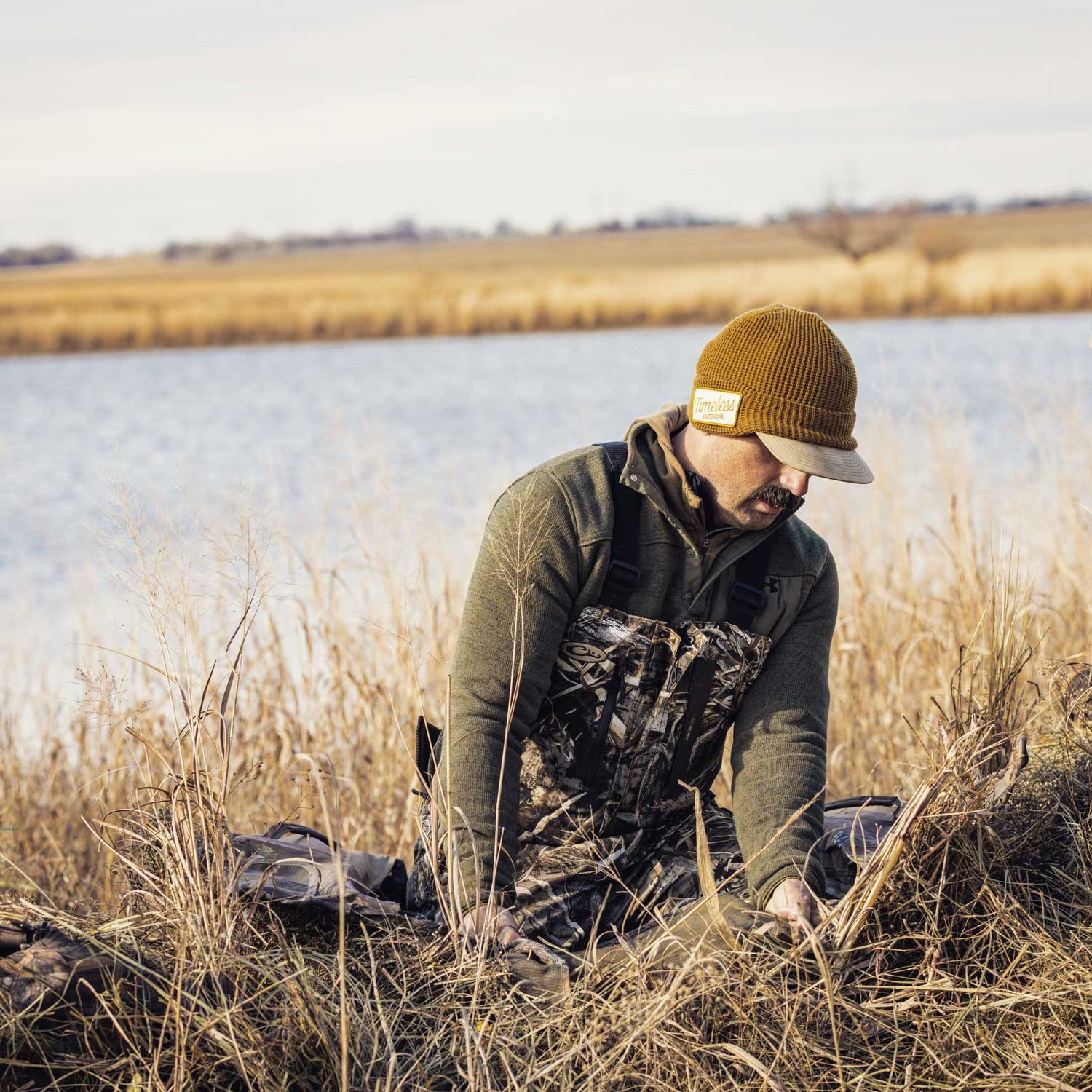 hunter wearing camo tending to his gear in the grass