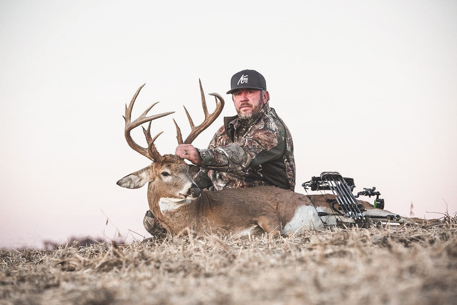 hunter sitting down in a field and holding up the antlers of a male white-tail deer he shot while hunting