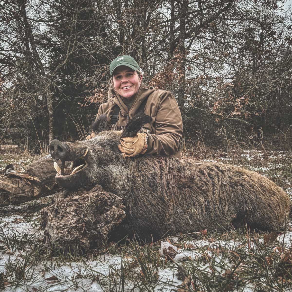woman sitting on the ground and holding onto a large wild boar she shot while hunting